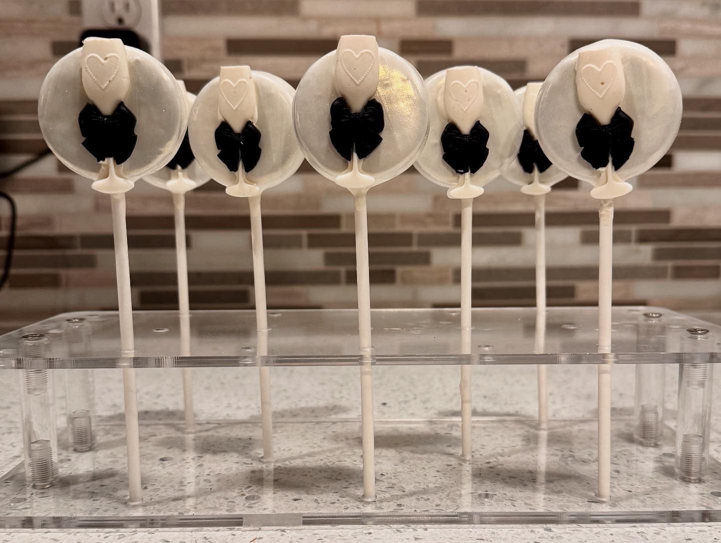 Cream chocolate lollipops, each with a small heart charm and black bow, on white sticks.