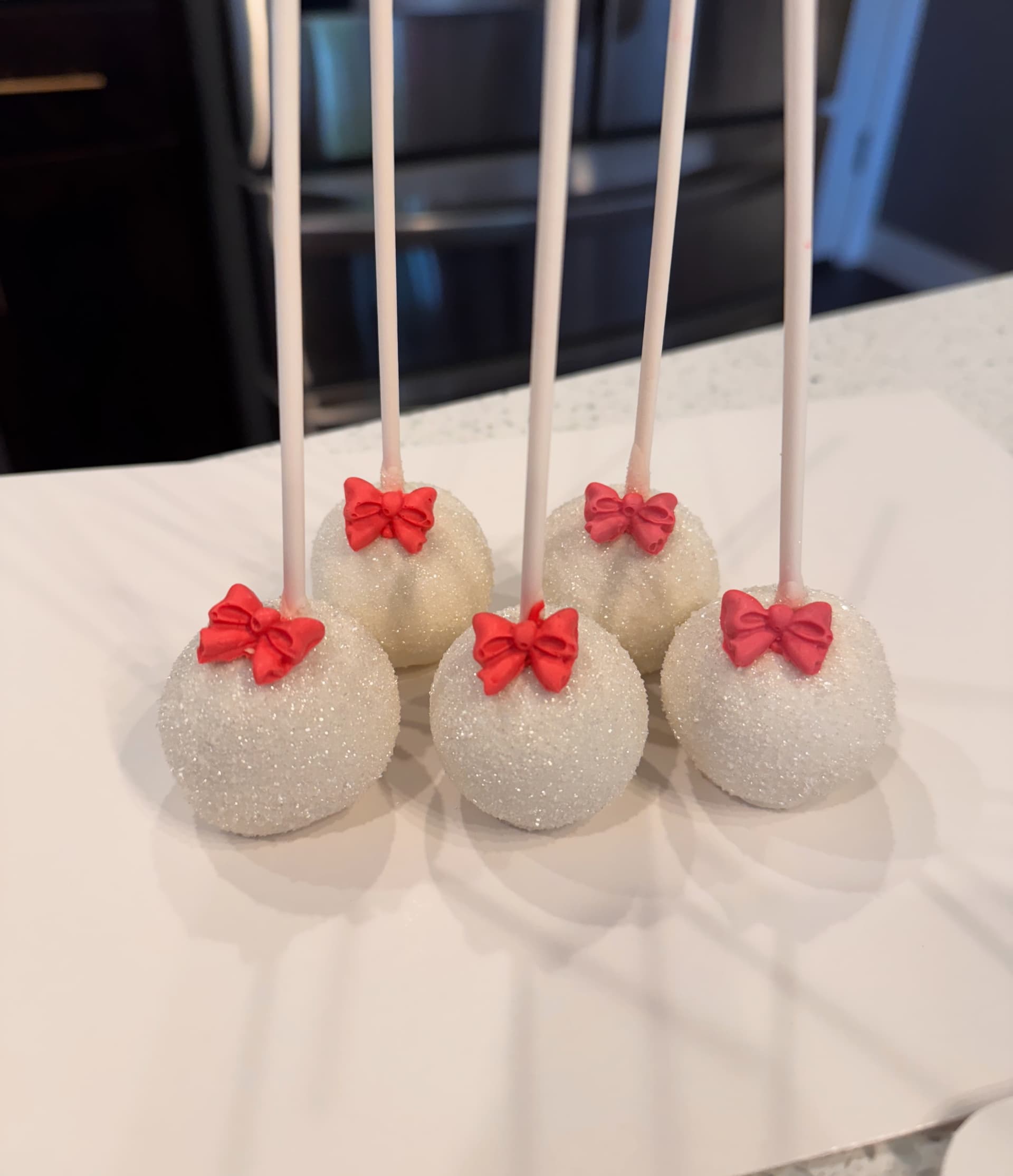 White cake pops rolled in sparkling sugar, each topped with a small red fondant bow.