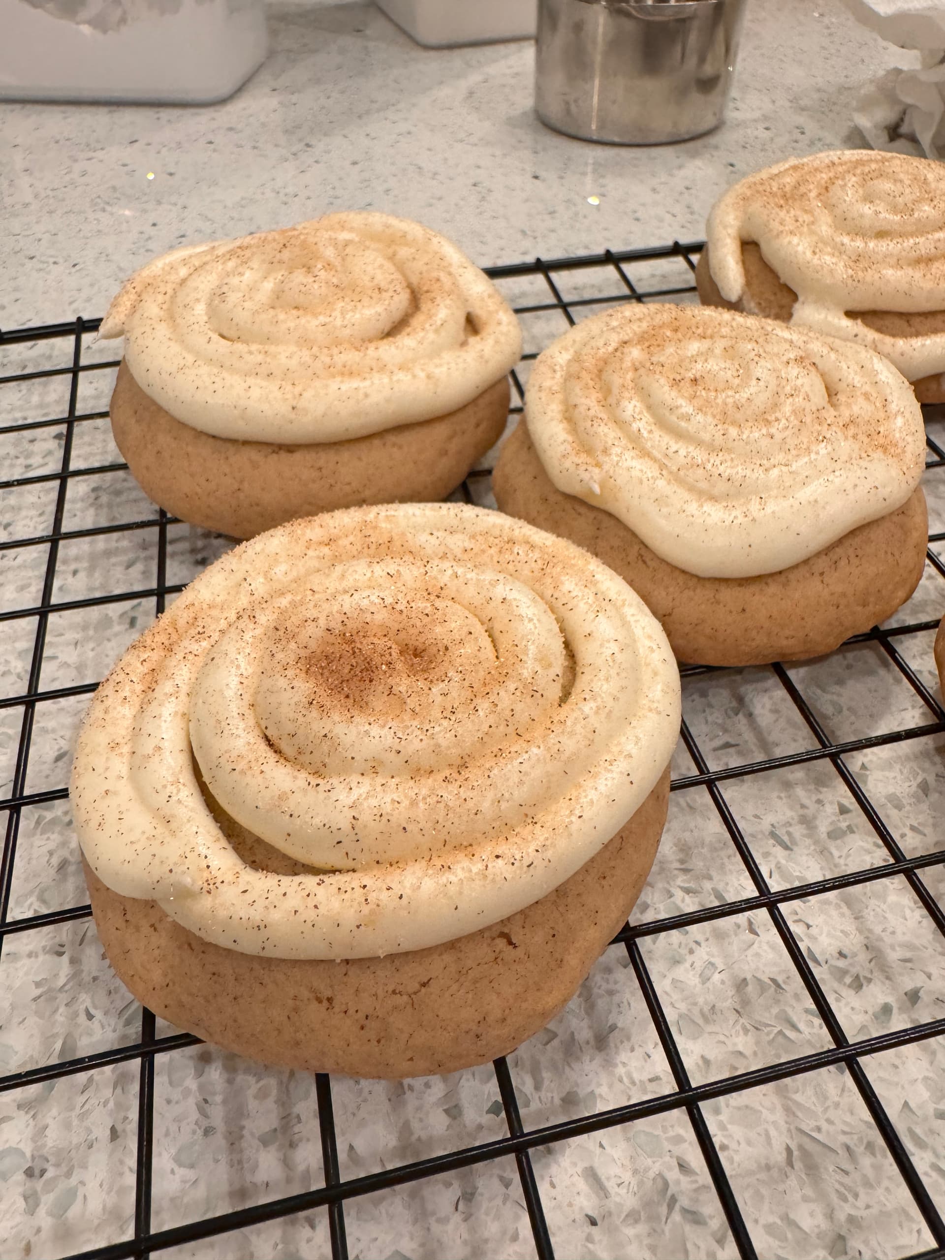 Cinnamon-roll-shaped sugar cookies dusted with cinnamon, cooling on a wire rack.
