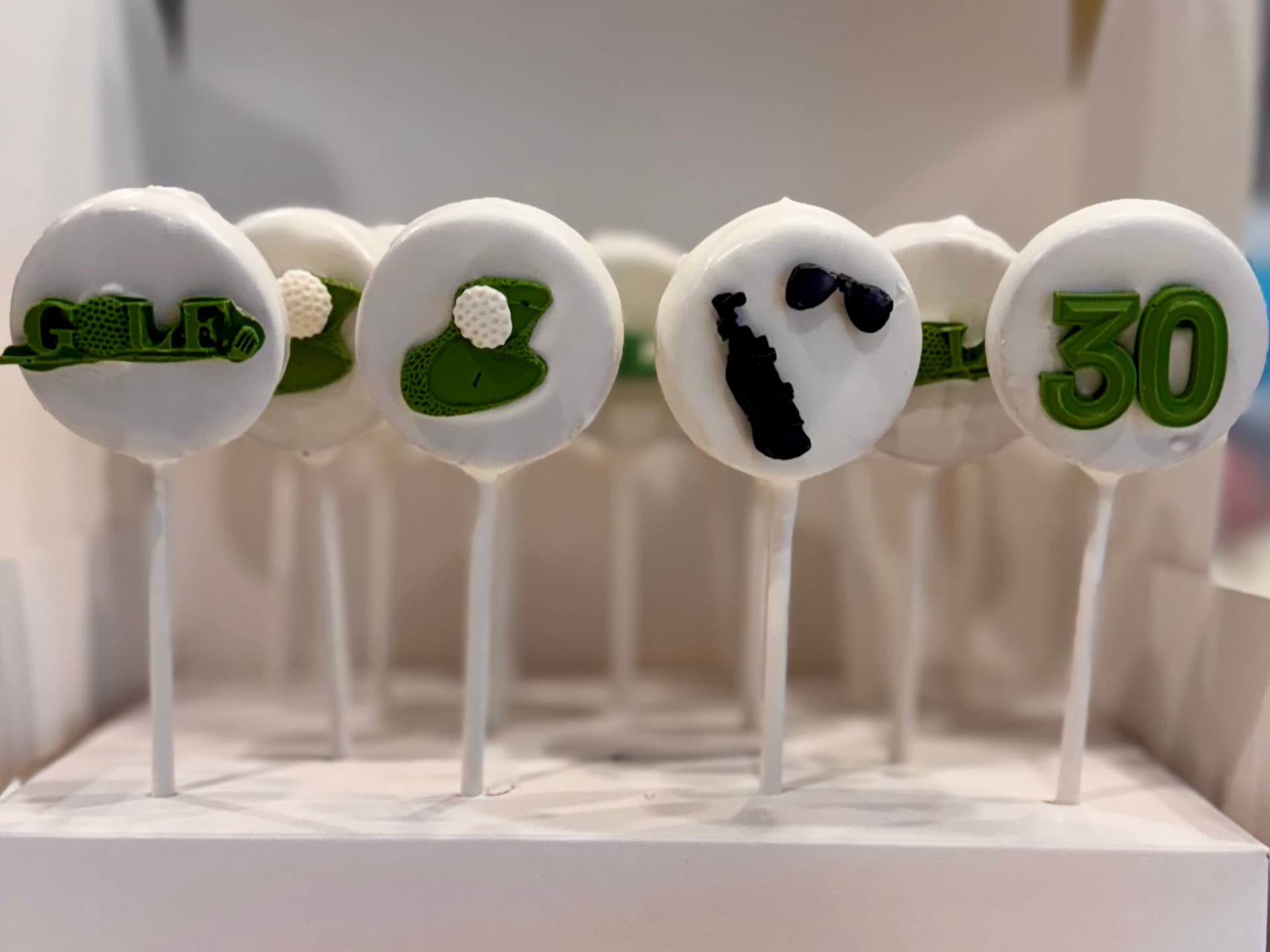 Golf-themed cake pops with a putting green, golf clubs, sunglasses and the number 30, on a stand.