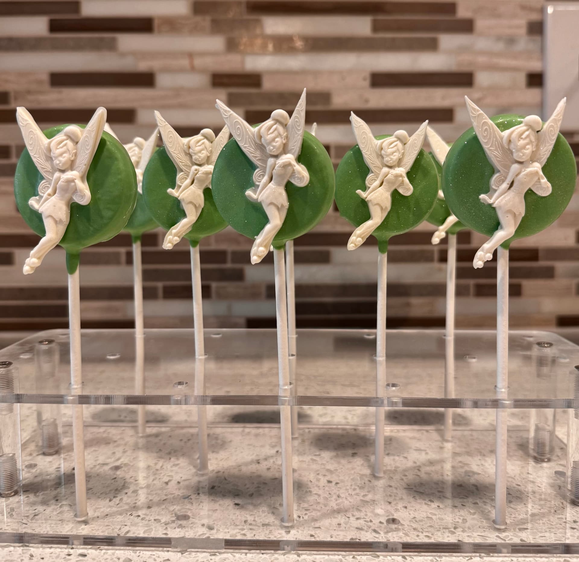 Cake pops with a black-and-white monogram letter S ringed in black nonpareils, on a stand.