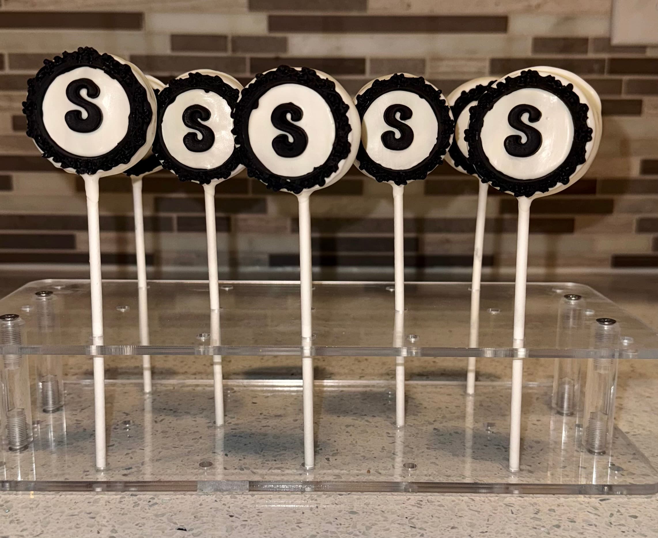 Cake pops with a black-and-white monogram letter S ringed in black nonpareils, on a clear stand.