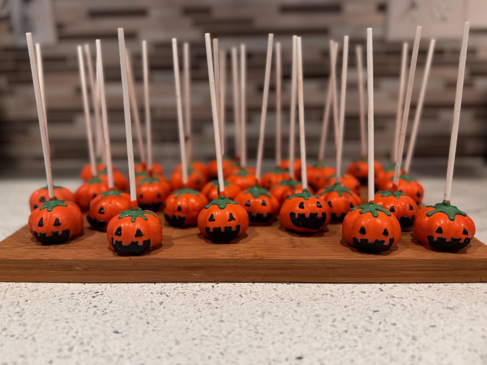 Strawberry-shaped red chocolate cake pops with white chocolate seed detailing, clustered on a wood board.