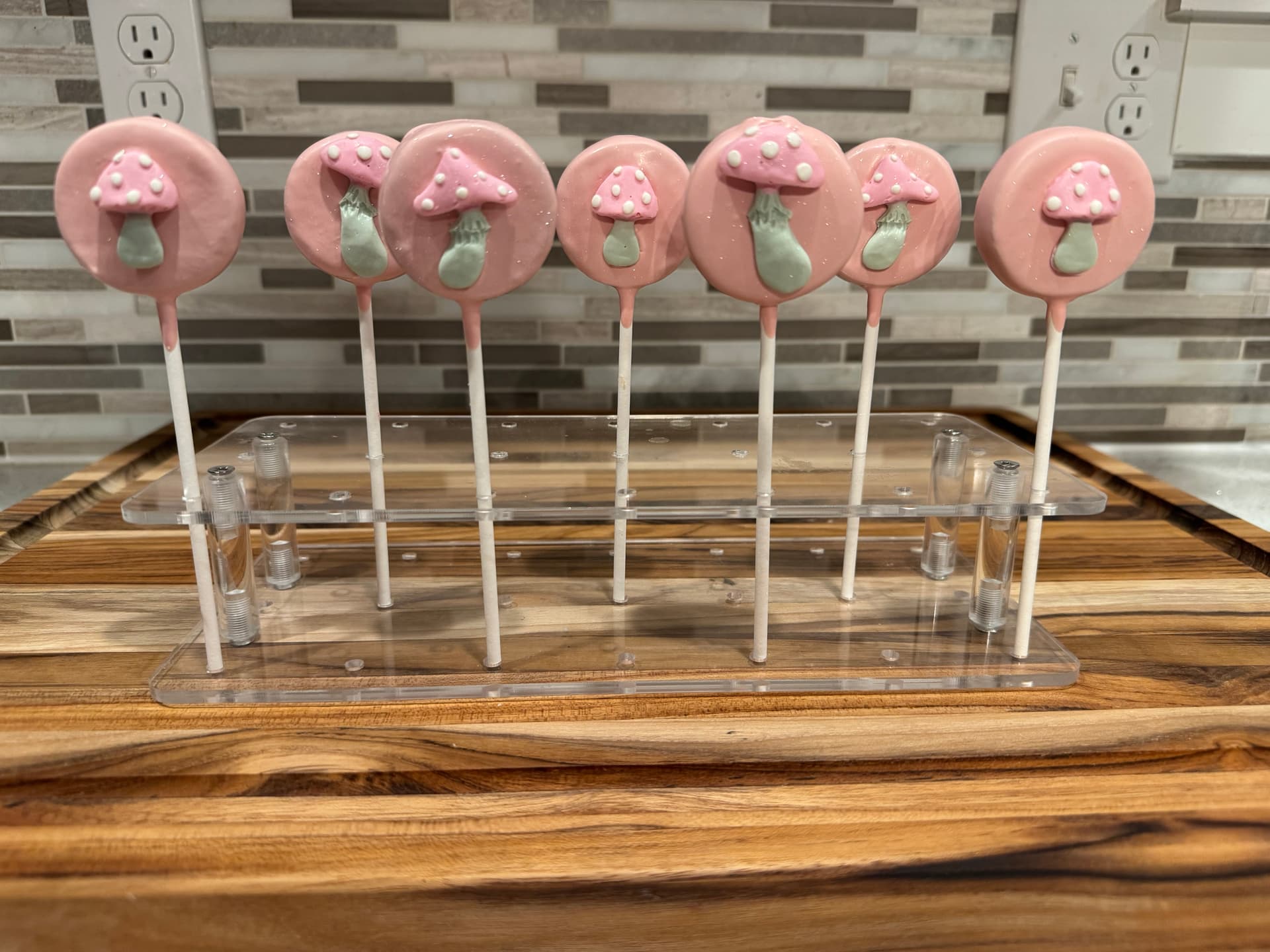 Strawberry-shaped cake pops with white chocolate seed detail, hanging from a stand.