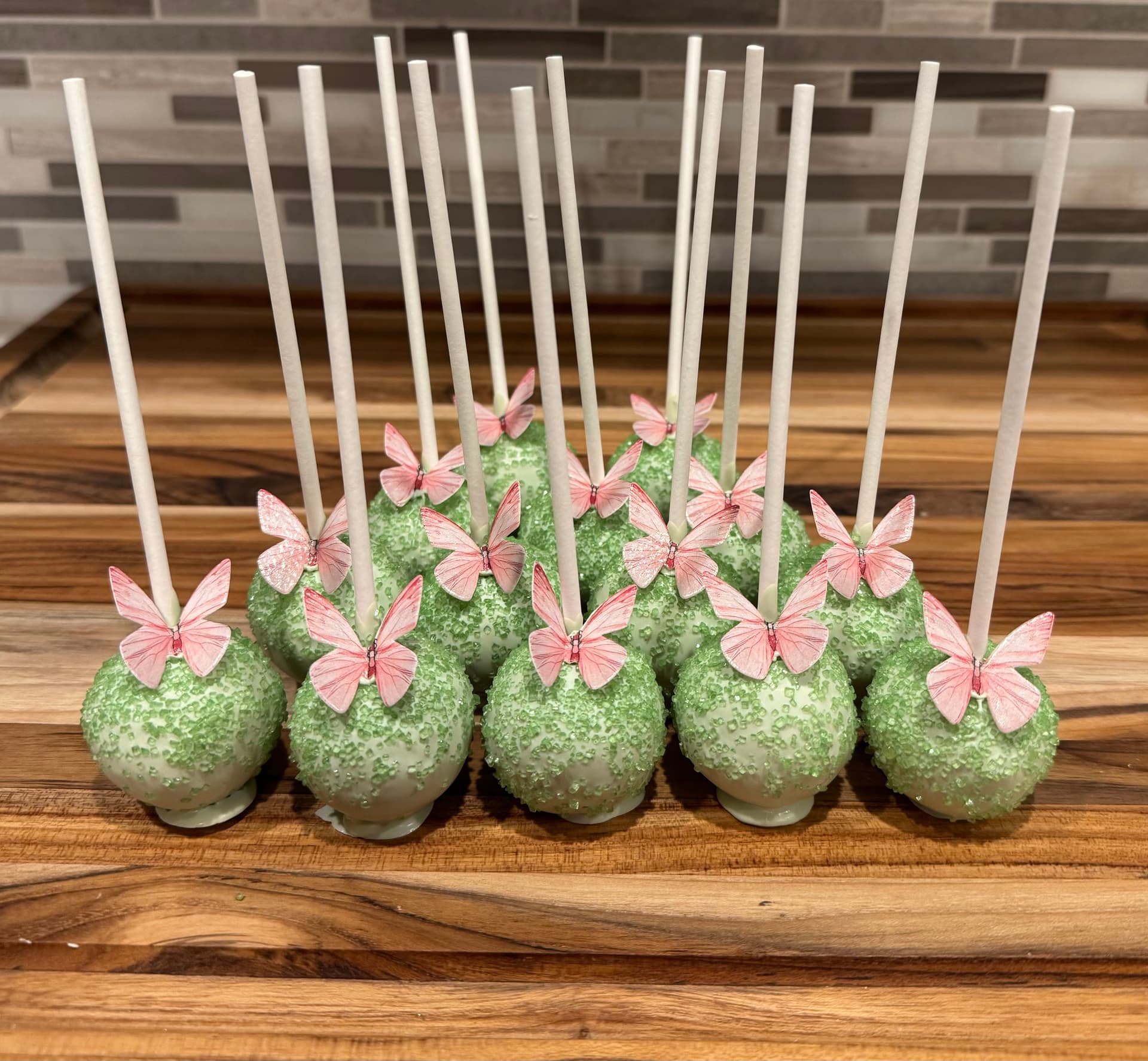 Pink cake pops with ornate picture-frame and butterfly wafer decorations, each centered on a small fondant rose.