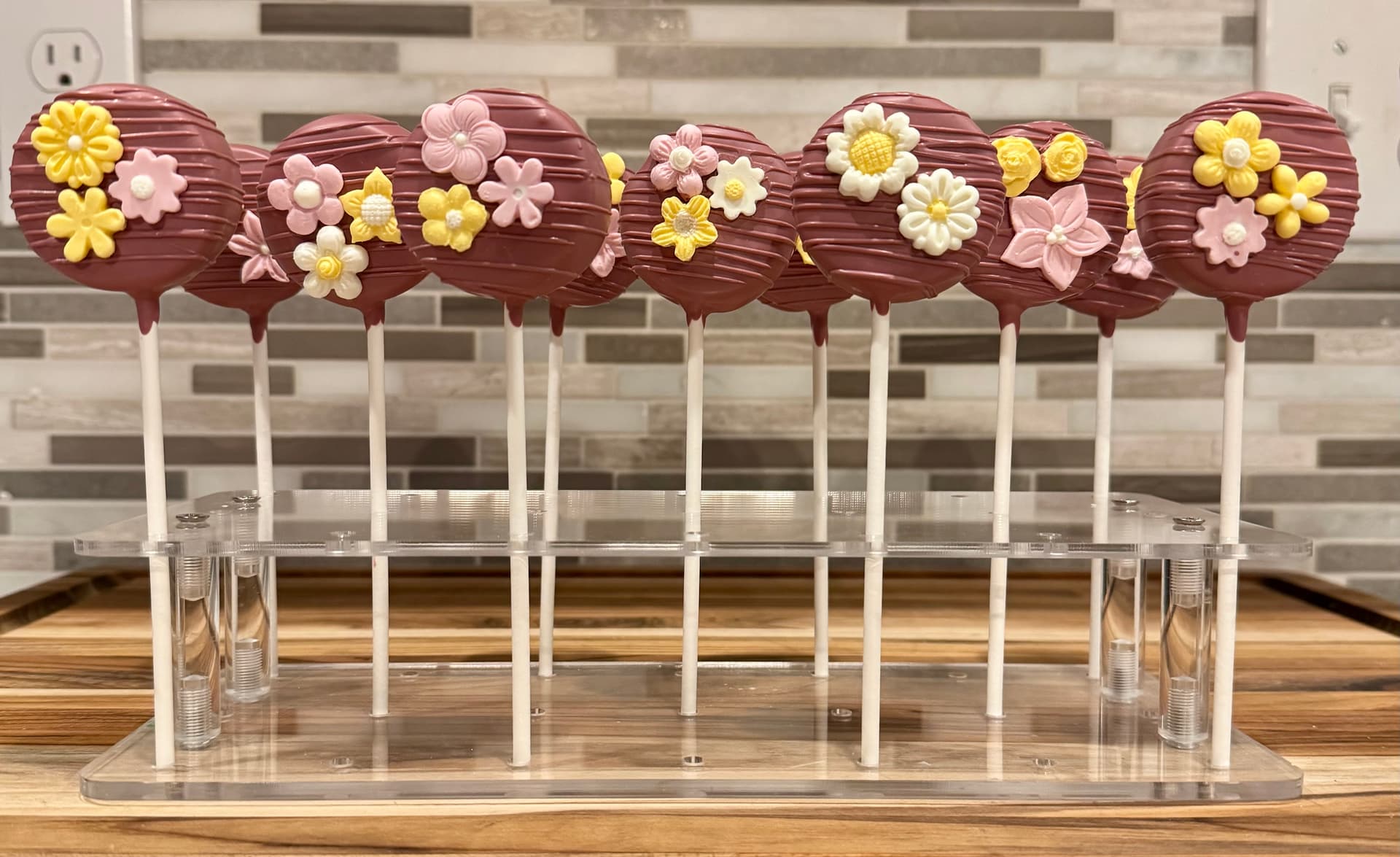 Maroon cake pops with clusters of fondant flowers in pink, yellow and white.