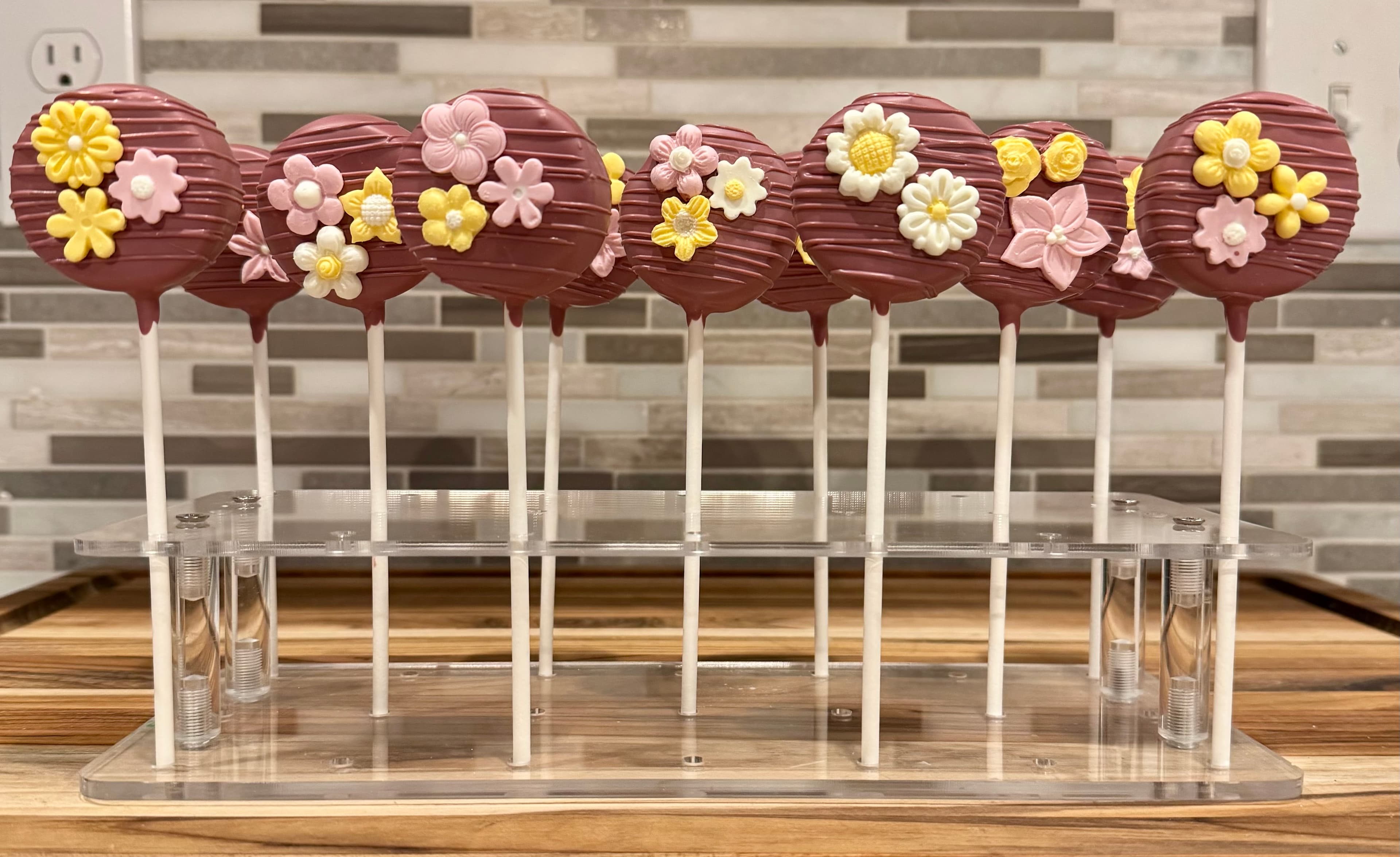 Maroon cake pops decorated with clusters of pink, yellow and white fondant flowers.