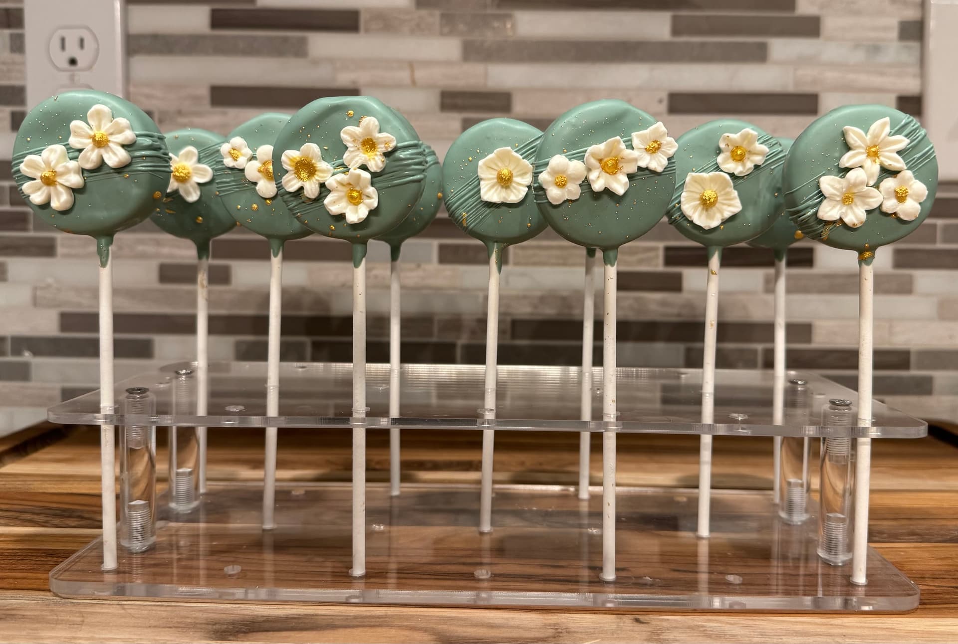 Sage green cake pops decorated with small white fondant flowers with gold centers and gold leaf flecks.