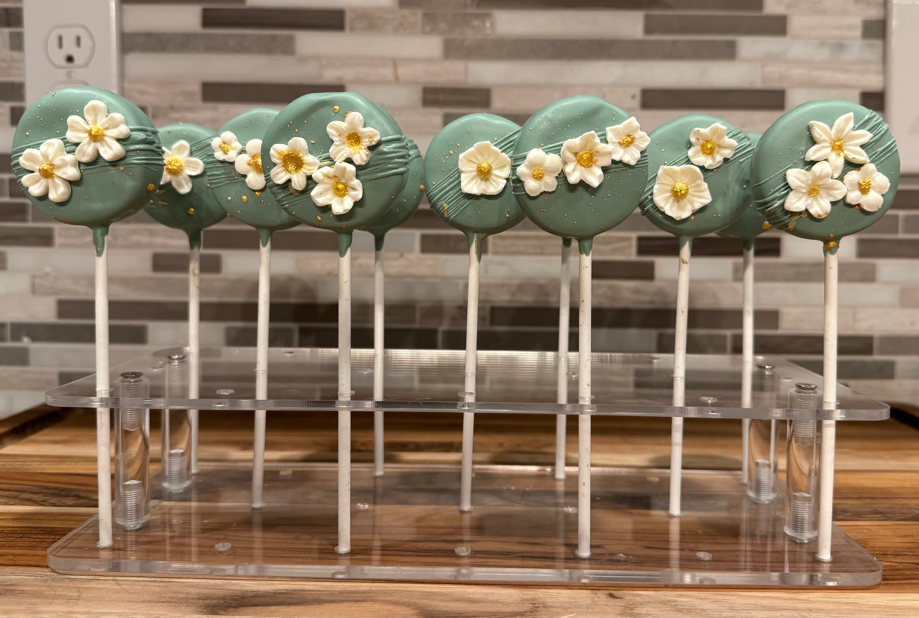 Sage green cake pops decorated with small white fondant flowers with gold centers.