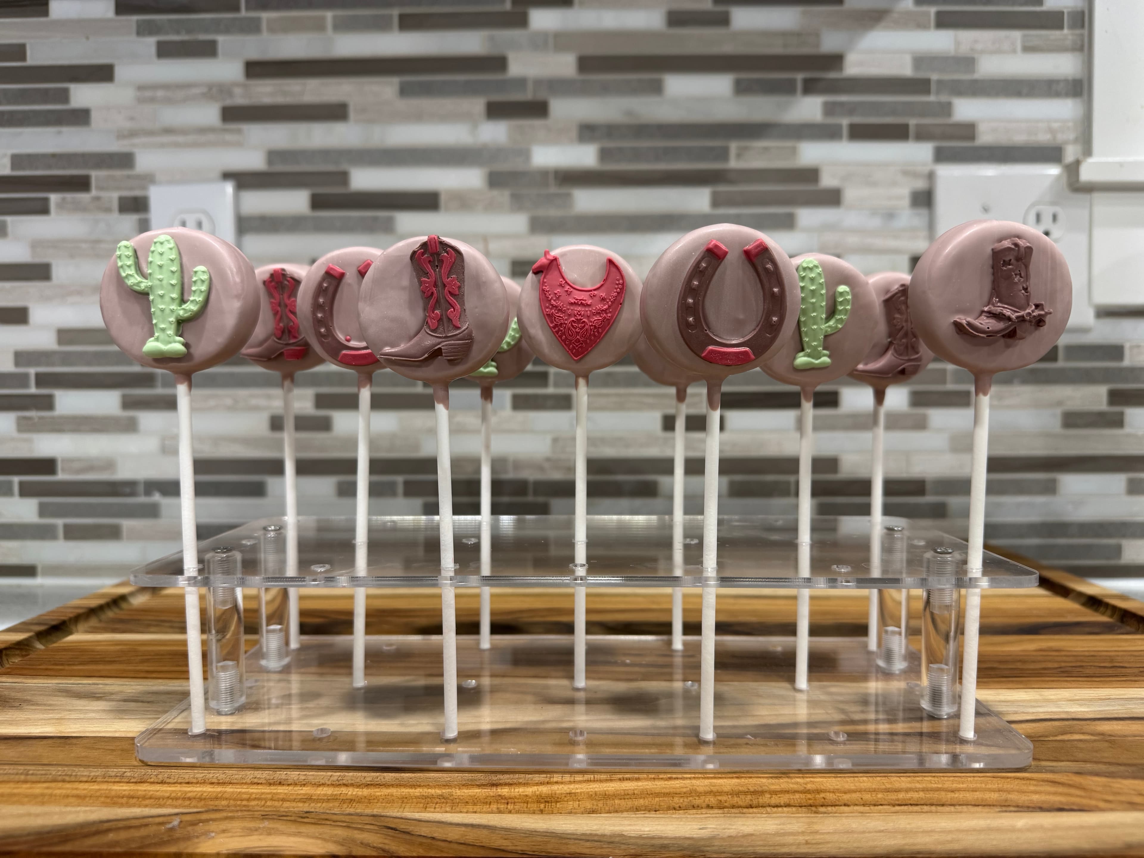 Pink western cake pops with fondant hats, boots, horseshoes and cactus, hung to set.