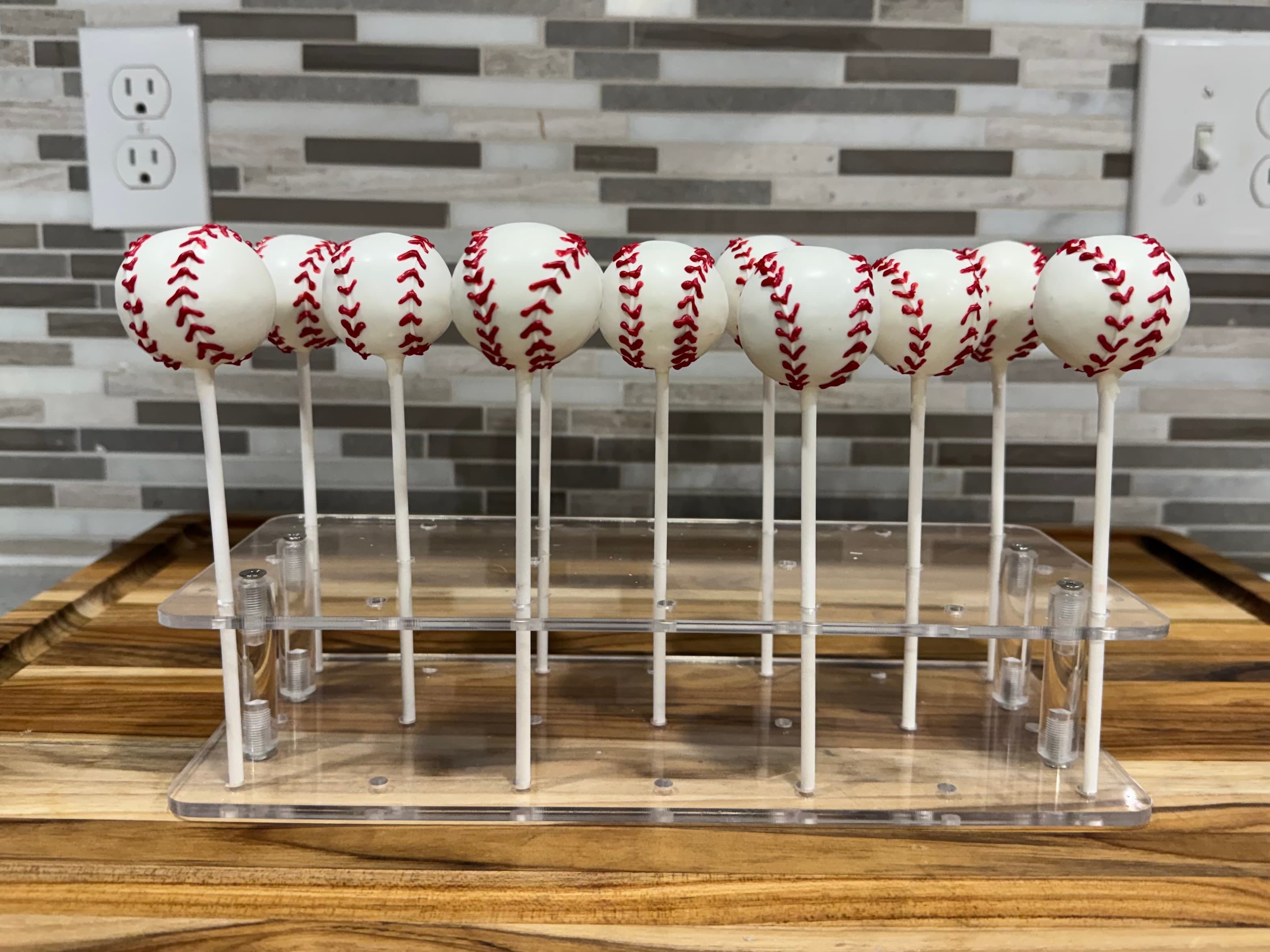 White cake pops piped with red baseball stitching, on a clear stand.