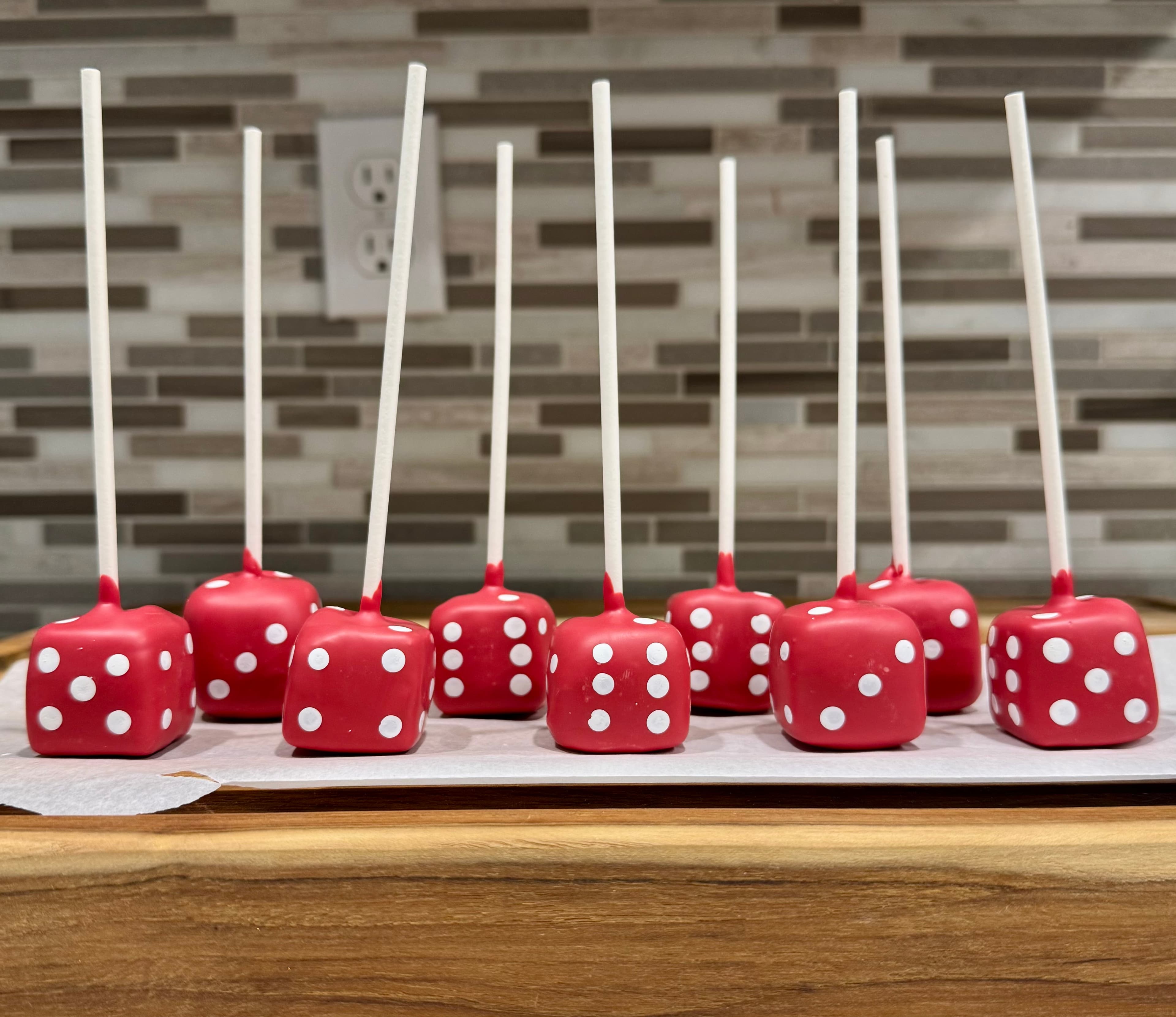 Red dice cake pops with white pips, on a wood board.